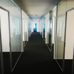 Großer Flur mit vielen Büros links und rechts durch Glastrennwände getrennt